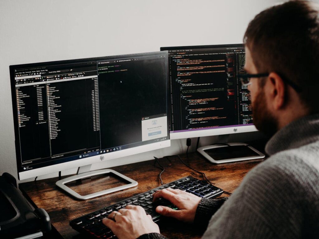 Man coding in front of two computer screens.