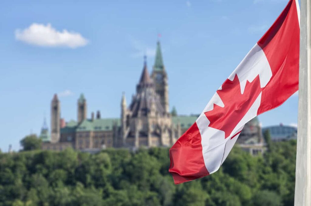 Canadian flag with government buildings in background.